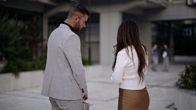 Two business professionals discuss content on a tablet outside a modern corporate building, then walk away. Ideal for themes of teamwork, urban business, and technology in the workplace.