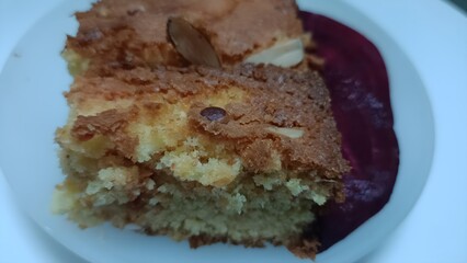 Close-up of a moist beetroot cake slice topped with almonds, served with fresh beetroot slices on a white plate. The golden crumb and vibrant color highlight healthy homemade baking and natural sweetn