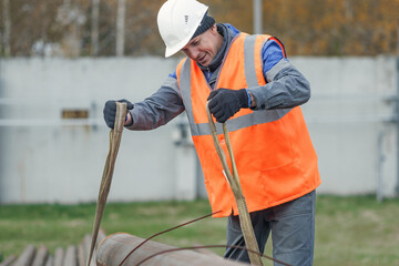A construction worker in an orange vest and hard hat is securing materials at a job site. The setting is outdoors with a focus on safety and teamwork.