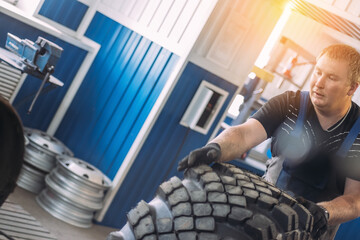 A worker in a tire shop handling a large tire, surrounded by tools and equipment. The setting is...