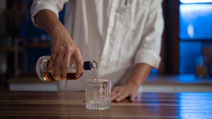 Man pouring whiskey into glass at night, warm light mood of relaxation and reflection.