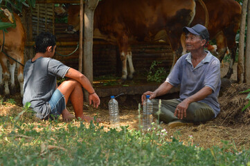 In the quiet afternoon, a farmer father smokes while watching his field with relief, as his son sits beside him near the barnyard in the village farm.