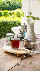 A tranquil scene of Vietnamese drip coffee or tea on a rustic wooden table with a white plant vase and lush green outdoor background