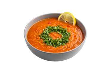 Red lentil tomato soup served with parsley and lemon on a gray plate against a white background. It's a vegetarian meal.