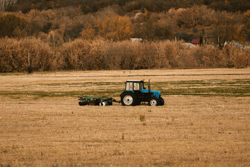 Fototapeta premium blue tractor drives across an autumn field, copy space