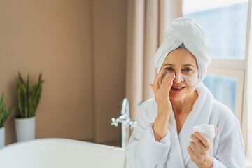 Mature adult old woman applying nourishing anti age face cream doing daily beauty routine. Senior...