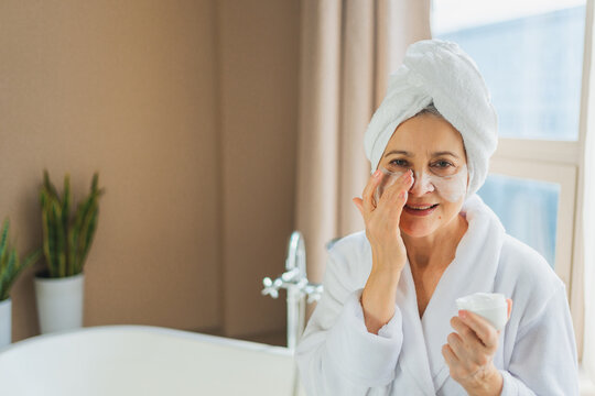 Mature adult old woman applying nourishing anti age face cream doing daily beauty routine. Senior woman with white mask or creme on skin gets facial treatment Skin care aging beauty skincare cosmetics