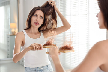 Woman with brush and lost hair near mirror at home. Alopecia problem