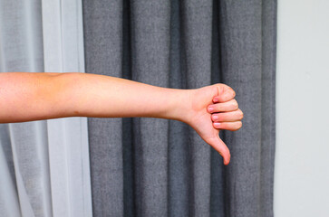 Human arm extended giving thumbs down gesture against modern gray curtain backdrop.