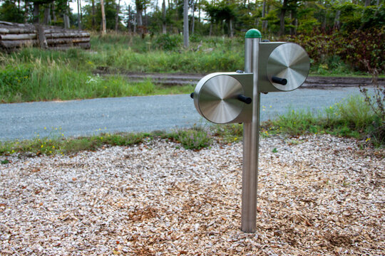 Outdoor fitness equipment featuring dual rotating discs on a sturdy metal frame, surrounded by natural greenery and gravel, promoting active lifestyle and exercise in a park setting