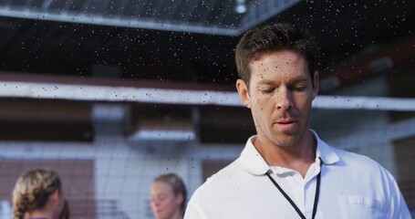 Standing coach in white polo instructing athletes on volleyball court with net droplets, copy space