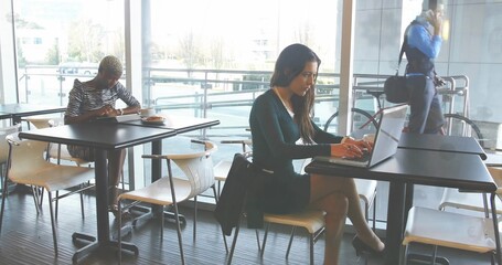 Typing businesswoman wearing dark dress working on laptop in lounge, with terrace view and bicycle