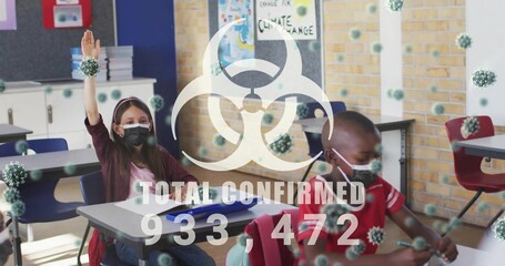 Raising masked girl hand and writing masked boy at desks in classroom, with biohazard overlay