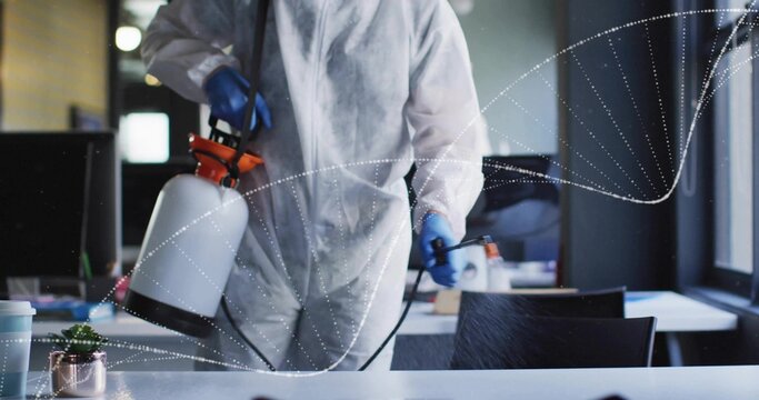 Spraying cleaning worker wearing protective suit disinfecting office desk, with sprayer and plant