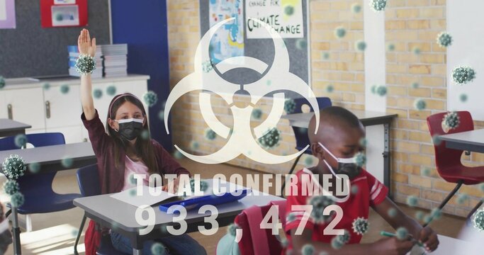 Raising masked girl hand and writing masked boy at desks in classroom, with biohazard overlay