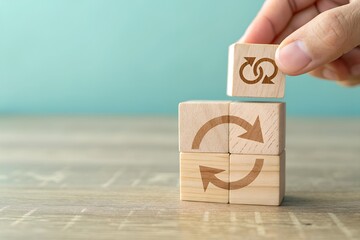 Hand stacking wooden blocks with circular arrow symbols representing recycling and sustainability