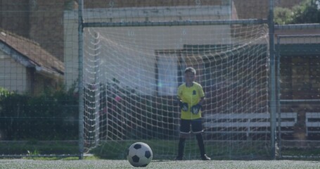 Child goalkeeper in yellow jersey and gloves guarding soccer goal on artificial turf, with ball