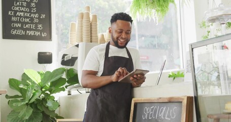 Operating tablet barista wearing apron at coffee counter, with espresso machine and chalkboard