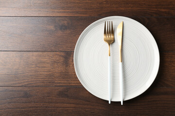 Clean ceramic plate and cutlery on wooden table, top view. Space for text