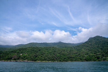 Lush tropical hills, mountains, and dense green forests stretch across the landscape under a partly...