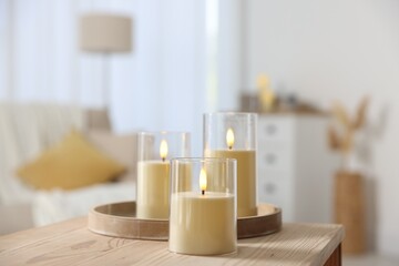 Decorative LED candles on wooden table at home, closeup
