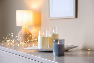 Decorative LED candles, pearl necklace, fairy lights and lamp on wooden cabinet indoors