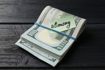 Note with word Alimony and money on wooden table, closeup