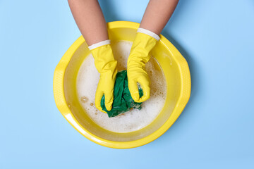 Woman washing clothes in plastic basin on light blue background, top view