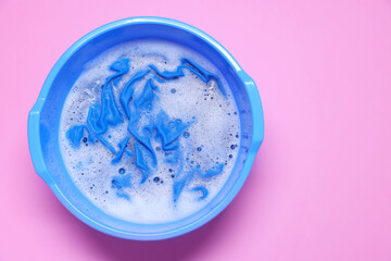 Plastic basin with clothes, water and foam on pink background, top view. Space for text