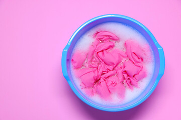Plastic basin with clothes, water and foam on pink background, top view. Space for text