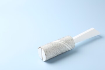 Lint roller with used sticky tape on light blue background, closeup. Space for text