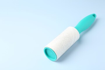 Lint roller with used sticky tape on light blue background, closeup. Space for text