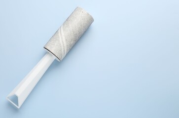 Lint roller with used sticky tape on light blue background, top view. space for text