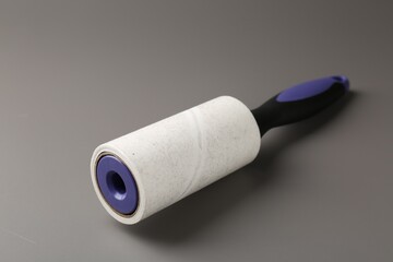 Lint roller with used sticky tape on grey background, closeup