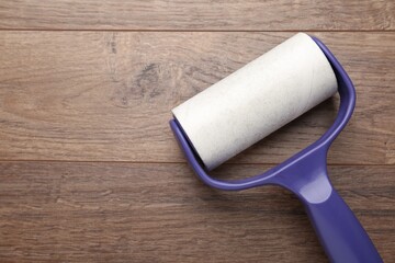 Sticky lint roller on wooden table, top view. Space for text