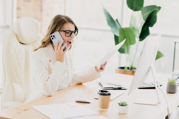 Professional businesswoman in formalwear working in a modern office, multitasking with a smartphone and paperwork