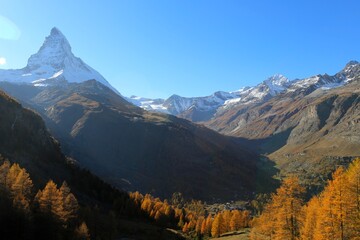 Golden autumn landscape with the Matterhorn above Zermatt, Switzerland. Snowy peaks, blue sky, and colorful larch trees.
