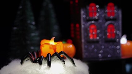 A yellow artificial candle in a spider-shaped candlestick against the backdrop of a rotating house and Christmas trees - Powered by Adobe