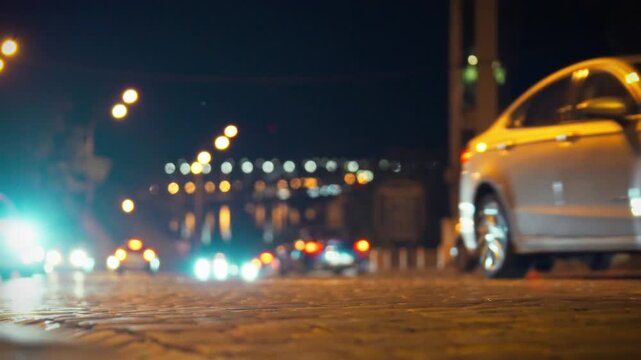 A group of vehicles drives along a cobblestone street at night, their headlights brightly illuminating the surroundings