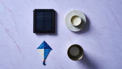 A Serene Still Life Composition Featuring a Solar Panel, Candle, Kite, and Metal Container on a Textured Lavender Surface, Evoking a Sense of Calm and Contemplation