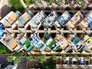 Aerial top-down view of colorful rooftop terraces, sunbeds, pergolas, and private spaces in a Mediterranean-style residential complex with palm trees in Cabo Roig, Costa Blanca, Spain.