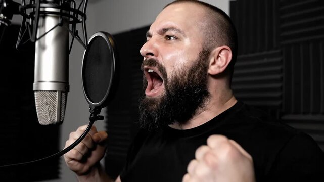 An Expressive Bearded Man Shouts Into A Condenser Microphone. He Is In A Recording Studio.