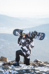 A snowboarder sits on his knee at the top of a mountain