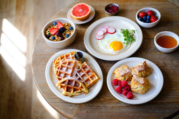 A Delicious Breakfast Spread Featuring Waffles, Eggs, Berries, and Pastries Arranged on a Rustic Wooden Tabletop for a Hearty and Nutritious Morning Meal