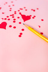 close-up of a number 2 pencil against a pink background with red and pink confetti and red cut-out hearts; Valentine's day crafting 