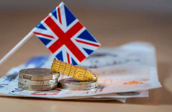 United Kingdom flag, pound banknotes, and coins featuring a miniature Big Ben representing economic challenges, debt crisis, and the financial impact of mild stagflation scenario on the UK economy