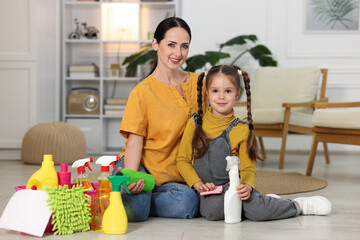 Little helper. Mother and daughter with different cleaning products and supplies on floor at home
