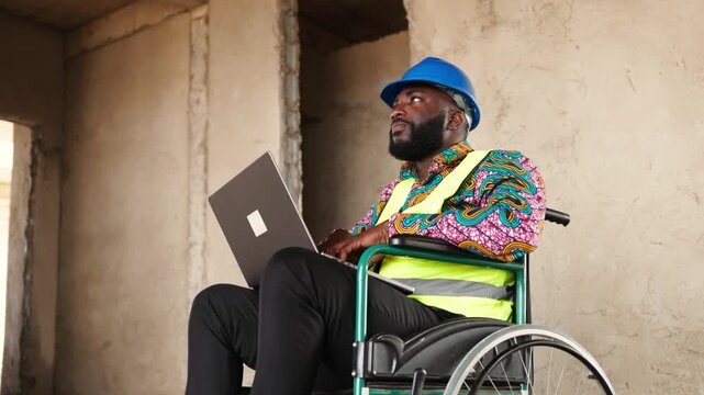 African construction engineer in a wheelchair, wearing a hard hat and safety vest working on a laptop at a building site