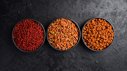 Black ceramic bowls with food for dogs and cats. On a black stone background. Free space for text.