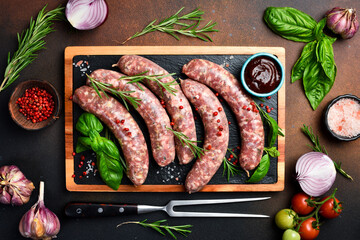 Raw beef sausages with rosemary and spices, ready to be grilled. On a wooden cutting board. Close...